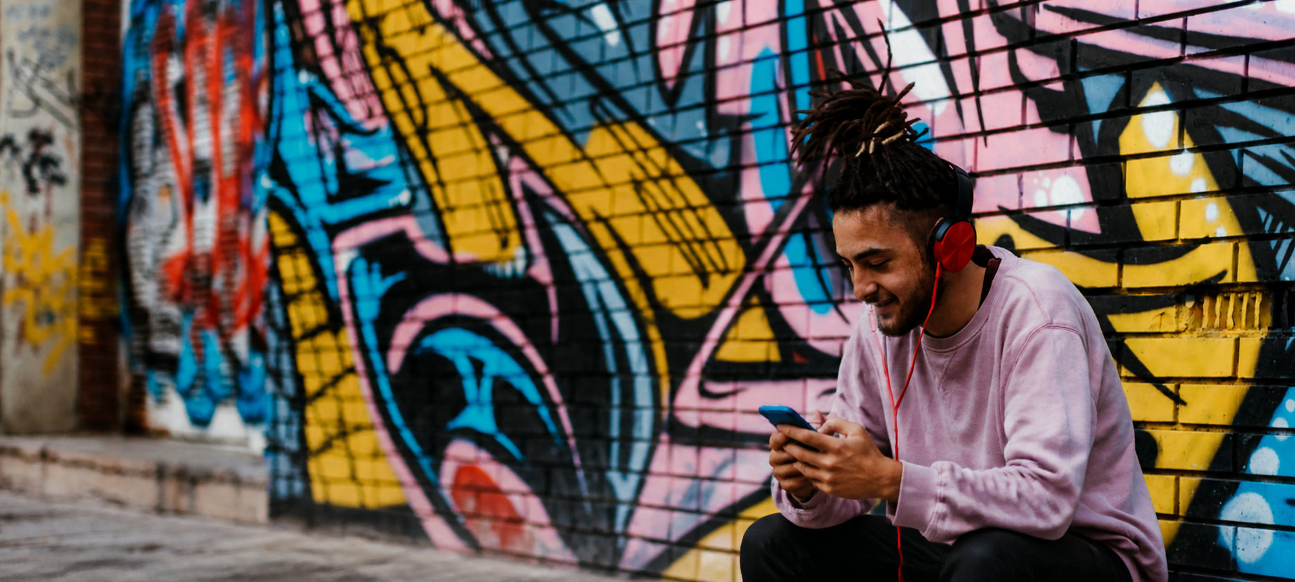 Élève souriant avec un casque audio devant un mur de graffitis colorés
